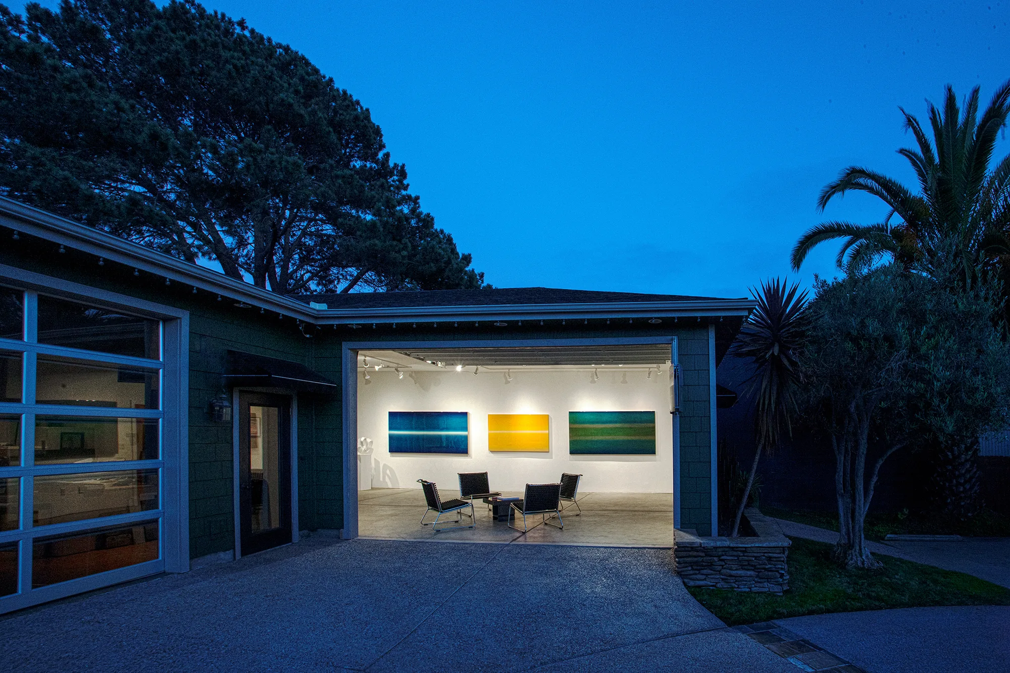 Susan Street Fine Art at dusk — the open gallery showing three luminous color-band paintings by Udo Nöger under track lighting.