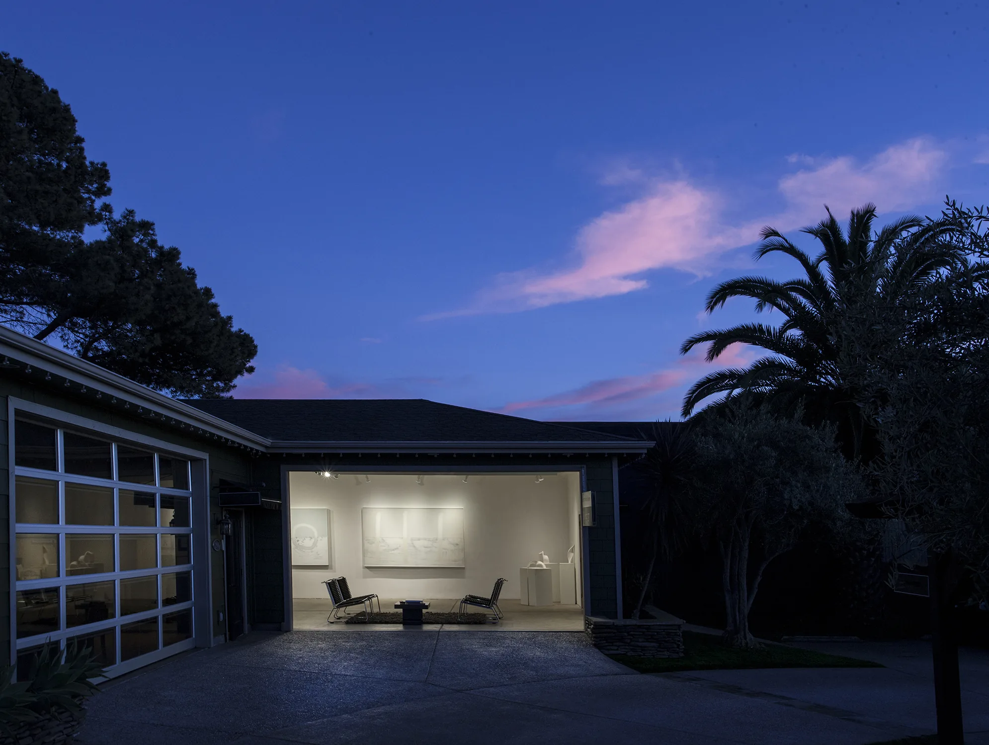 Susan Street Fine Art at dusk — the illuminated gallery glowing through the open front under a pink twilight sky.