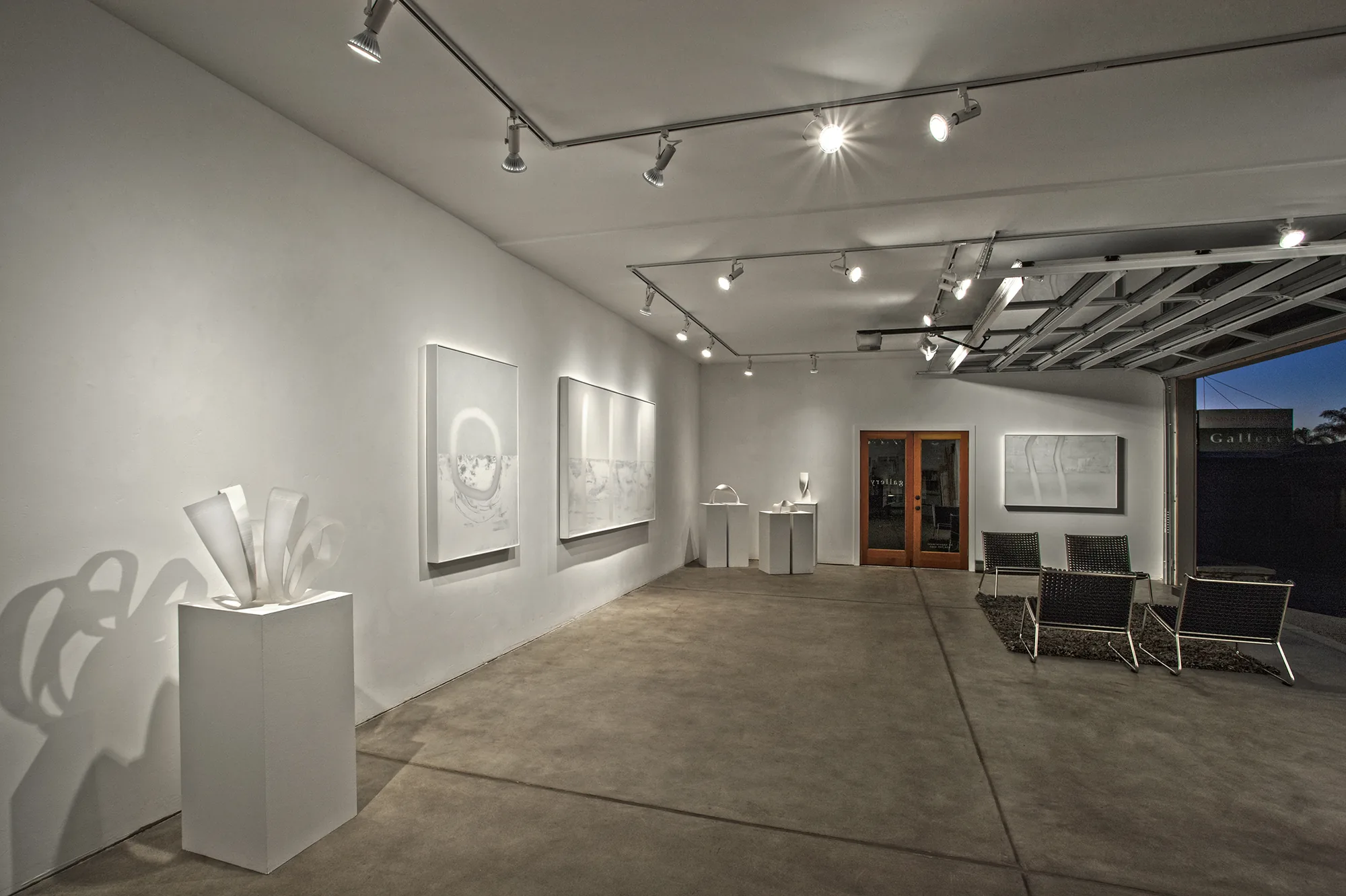 Inside Susan Street Fine Art — Udo Nöger works and a paper sculpture under gallery lighting, the front opening to dusk.